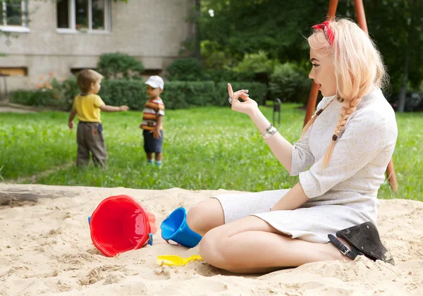Όμορφη νεαρή κοπέλα κάθεται στο sandbox για παιδιά. — Φωτογραφία Αρχείου