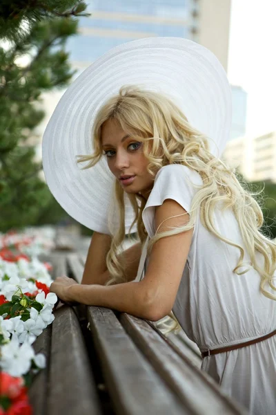 Retrato de mulher loira bonita em chapéu retro branco situado perto do parque — Fotografia de Stock