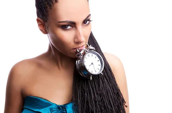 Emotional beautiful mulatto girl holds an alarm clock in a teeth. — Stock Photo, Image