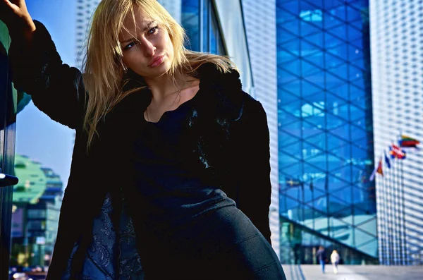 Beautiful blonde near a modern building from glass — Stock Photo, Image
