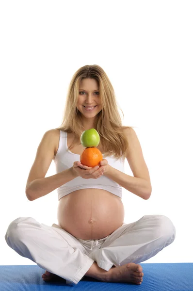 Zwangere vrouw die yoga beoefent en fruit houdt — Stockfoto