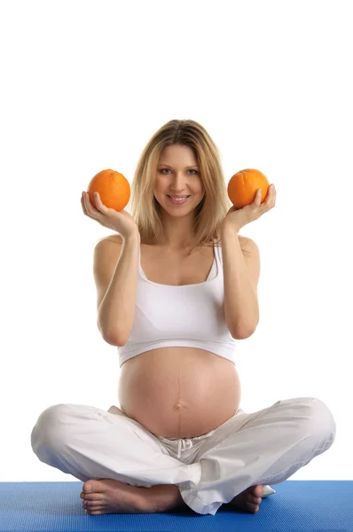 Беременная женщина занимается йогой и держит апельсины — стоковое фото