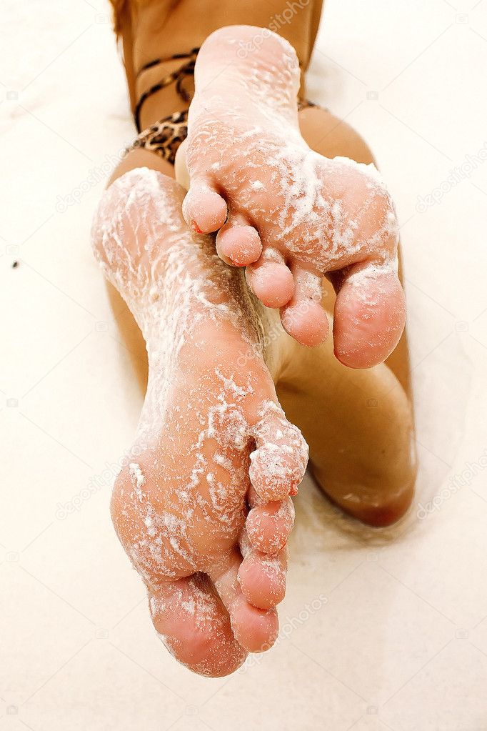 Foot of young woman laying on a white sand