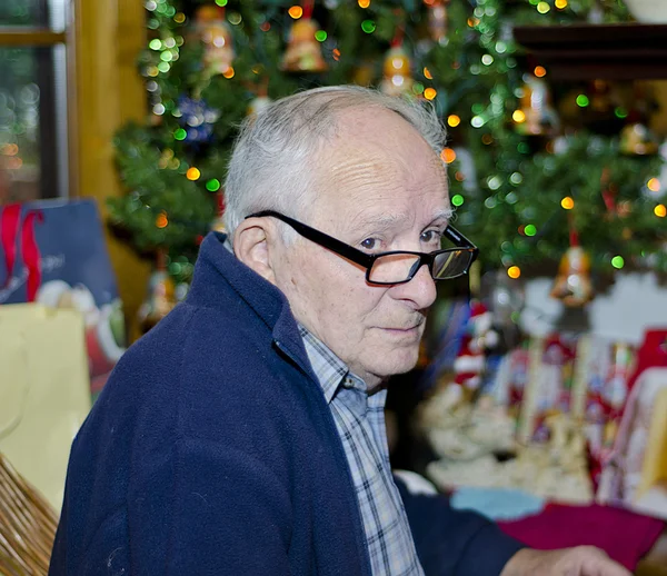 Oude man ontspannen in de buurt van een kerstboom — Stockfoto