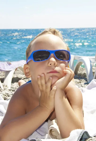 A fiú egy napszemüveget sunbathes a strandon — Stock Fotó