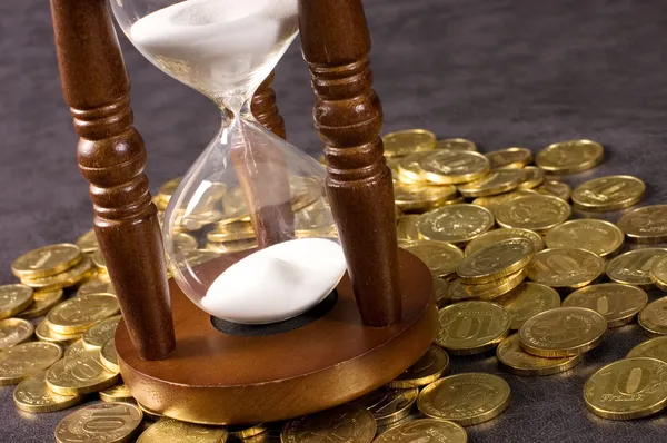 Timglas och mynt på en grå — Stockfoto