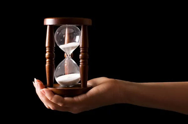 Hourglass in hands on a black — Stock Photo, Image