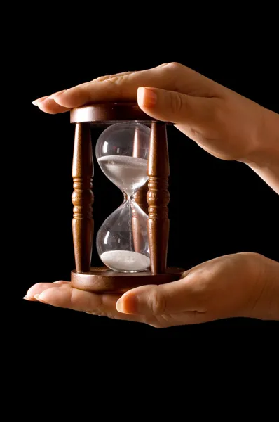 Песочные часы в руках на черном — стоковое фото