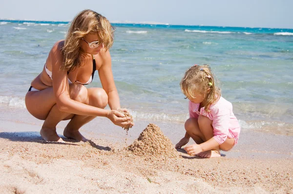 Mãe com a criança brincando com areia na praia — Fotografia de Stock