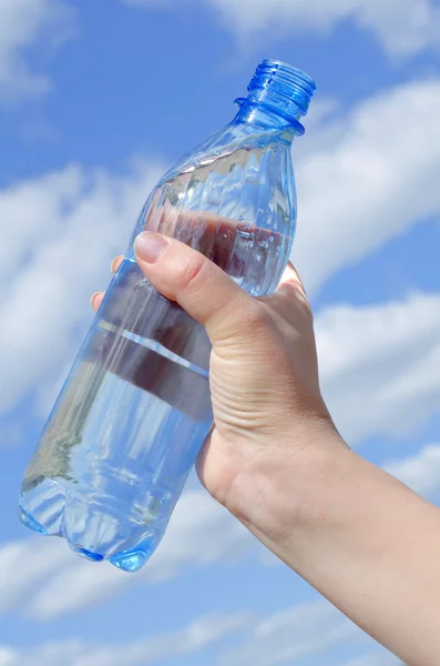 Láhev s vodou do ruky proti obloze — Stock fotografie