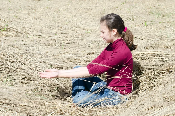Meisje zit op een droog gras — Stockfoto