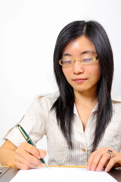 Chinesische Geschäftsfrau sitzt am Schreibtisch und schreibt Stockbild