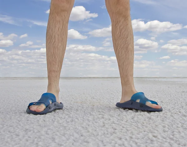 Opálené nohy člověka nosí žabky, stojící na pláži — Stock fotografie