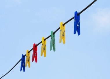 Colorful clothes pegs hanging in the line wire over blue sky clipart