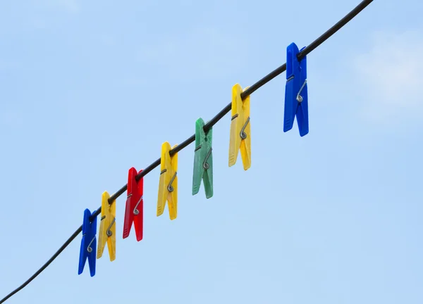 Barevné kolíčky na prádlo visí v linii drátu nad modrá obloha — Stock fotografie