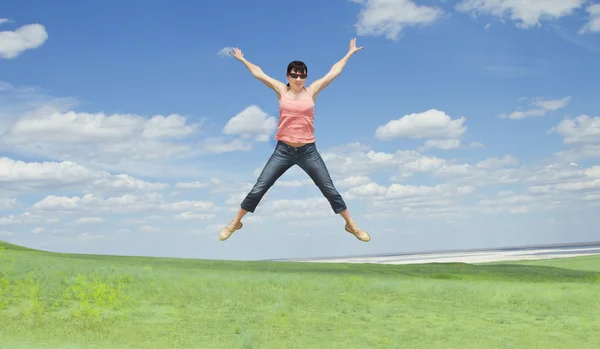Genç ve güzel kadın üzerinde yeşil çim üzerinde mavi gökyüzü atlama — Stok fotoğraf