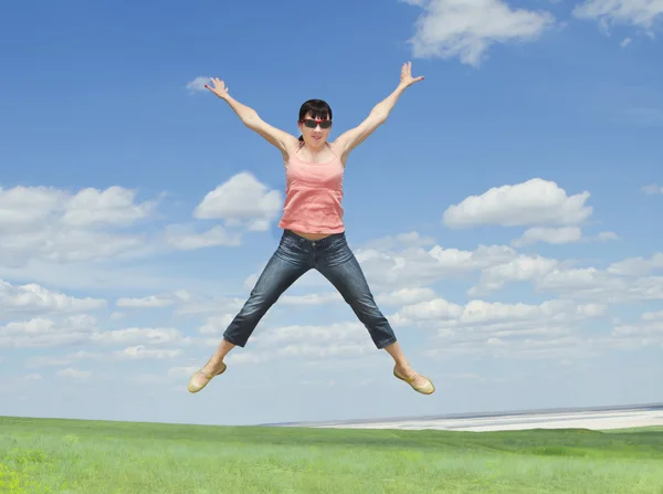 Pretty young woman jumping on green grass over blue sky — Stock Photo, Image