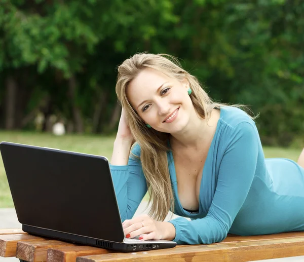 Giovane bella donna con computer portatile sdraiato sulla panchina in un parco — Foto Stock