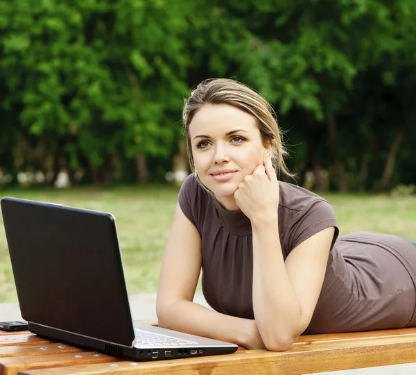 Ung vacker kvinna med laptop liggande på bänken på en park — Stockfoto
