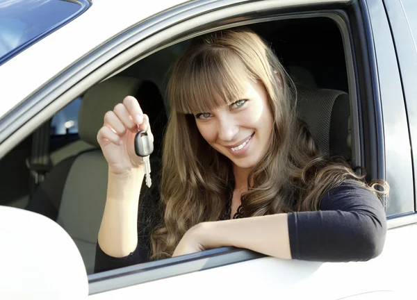 Veselá mladá dáma sedí v autě a ukazuje klíč — Stock fotografie