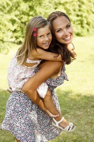Mother giving daughter piggy back ride at summer park — Stock Photo, Image