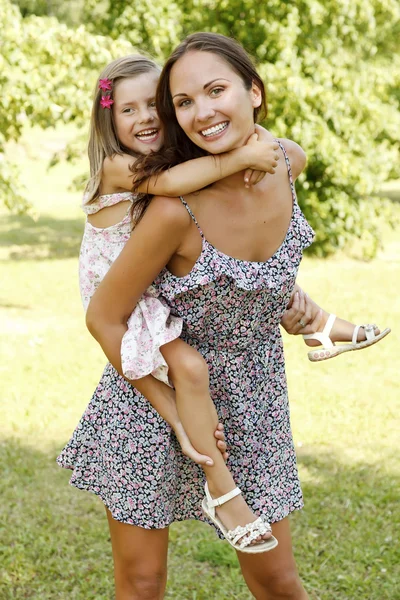 Mother giving daughter piggy back ride at summer park. — Stock Photo, Image