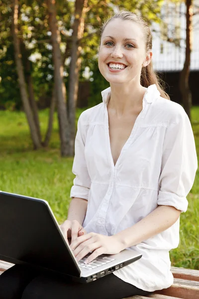 Güzel kadın bankta otururken dizüstü bilgisayar ile gülüyor. — Stok fotoğraf