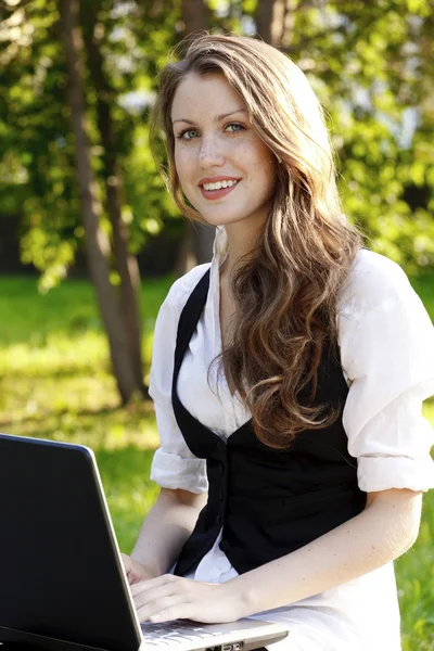 Jovem mulher bonita com laptop sentado no banco em um parque — Fotografia de Stock