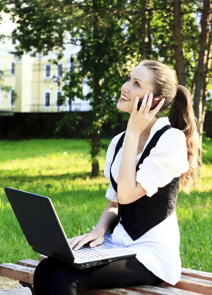 Jovem mulher bonita com laptop sentado no banco em um parque . — Fotografia de Stock