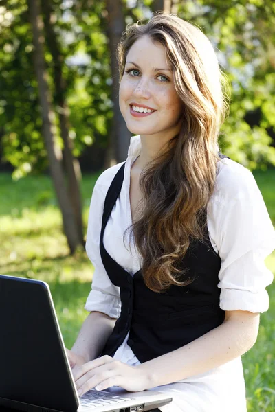 Jonge mooie vrouw met laptop zittend op de Bank in een park. — Stockfoto