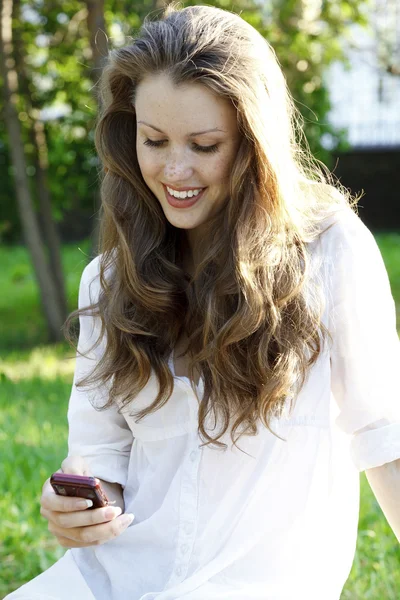 Ung kvinna läser sms på mobiltelefon — Stockfoto
