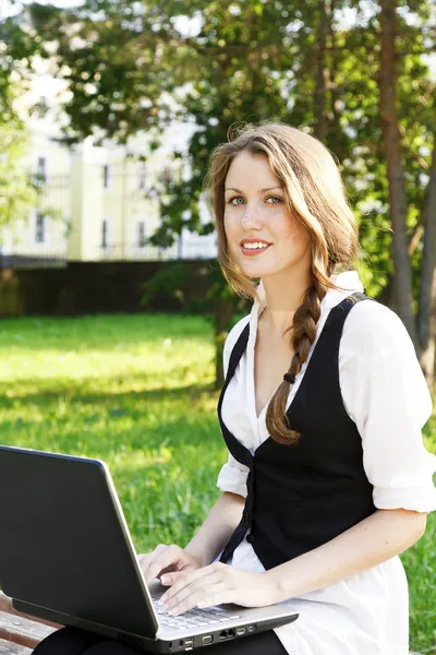 Ung vacker kvinna med laptop sitta på bänken i en park. — Stockfoto