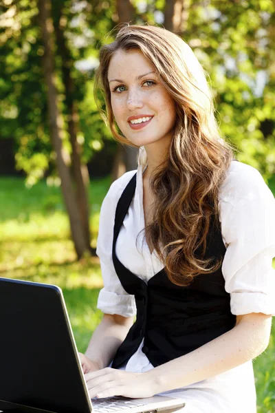 Jonge mooie vrouw met laptop zittend op de Bank in een park — Stockfoto