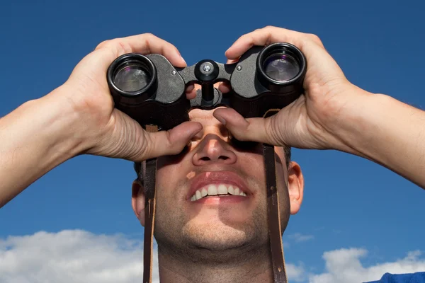 Young man looking with binoculars, blue sky — Stock Photo, Image