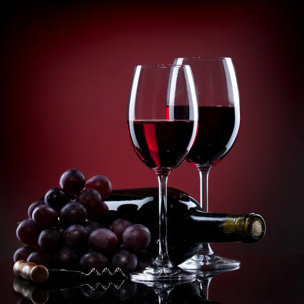 Vino in calici con uva e bottiglia su rosso — Foto Stock