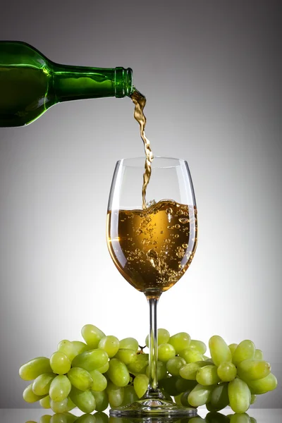 Vino blanco vertiendo en el vaso de botella con uva verde —  Fotos de Stock