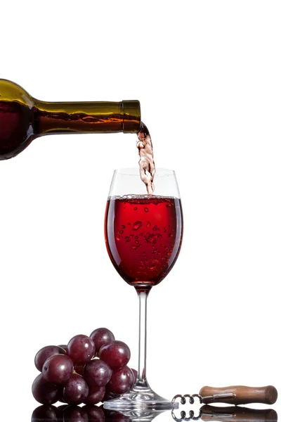 Red wine pouring into glass with grape isolated on white — Stock Photo, Image