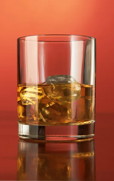 Whiskey with ice cubes on red — Stock Photo, Image