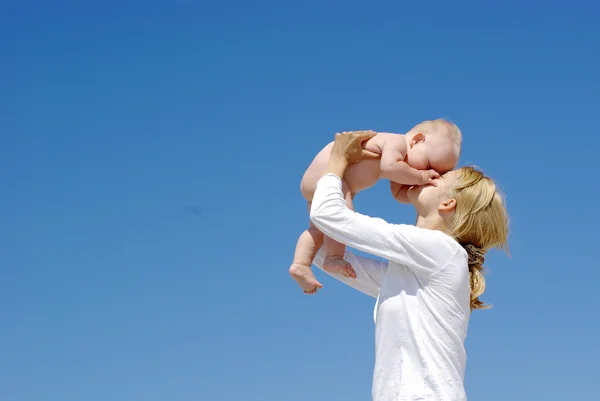 Mãe feliz e bebê brincando em um fundo céu azul — Fotografia de Stock