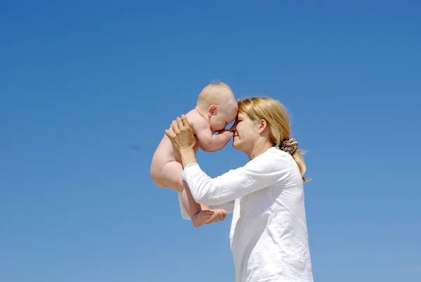Mère heureuse et bébé jouant sur un fond bleu ciel — Photo