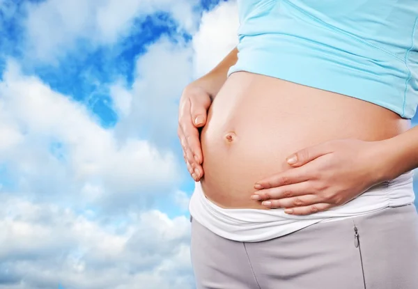 Bela barriga grávida sobre o céu nublado azul — Fotografia de Stock