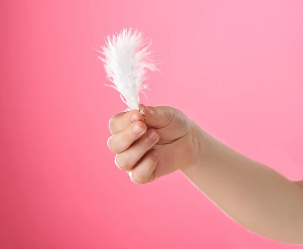 Child's hand holding white feather. Isolated on pink background — Stock Photo, Image