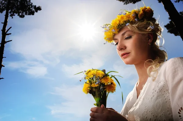Mulher bonita com flores de dente de leão sobre o céu azul — Fotografia de Stock