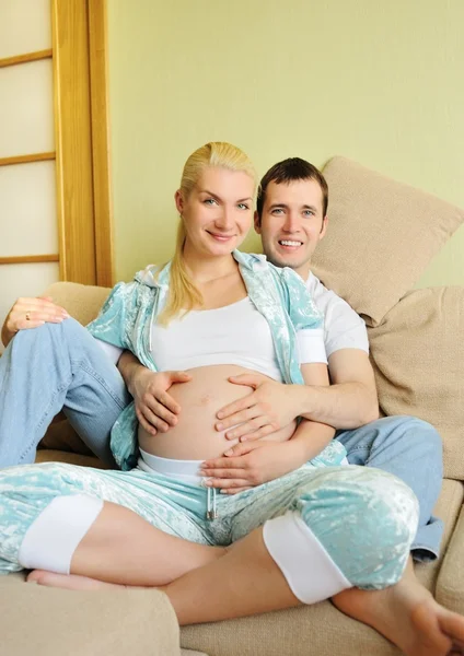 Krásná těhotná žena a muž sedí na gauči doma — Stock fotografie