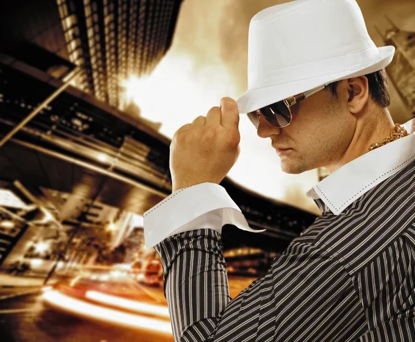 Homem elegante em um chapéu na frente da cidade da noite — Fotografia de Stock