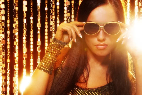 Atraktivní žena v sluneční brýle přes zlaté závěsy — Stock fotografie