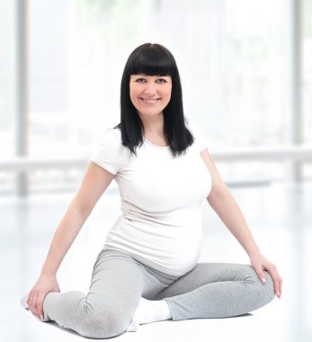 Pregnant woman sitting on the floor at an aerobics class clipart