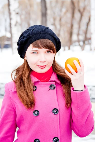 Mulher no inverno em um parque com laranja nas mãos — Fotografia de Stock