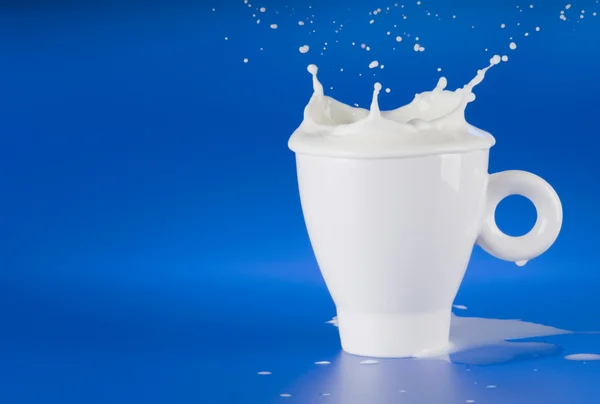 Milk splash out of white cup — Stock Photo, Image