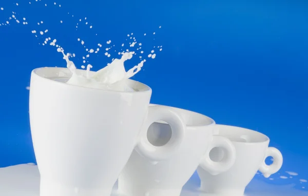 Milch spritzt aus weißem Becher — Stockfoto